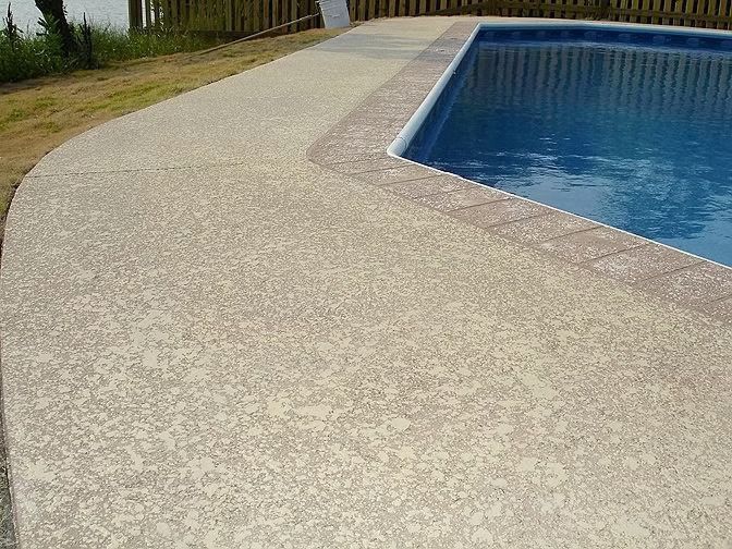 Curved beige pool deck beside a blue swimming pool with a brown border