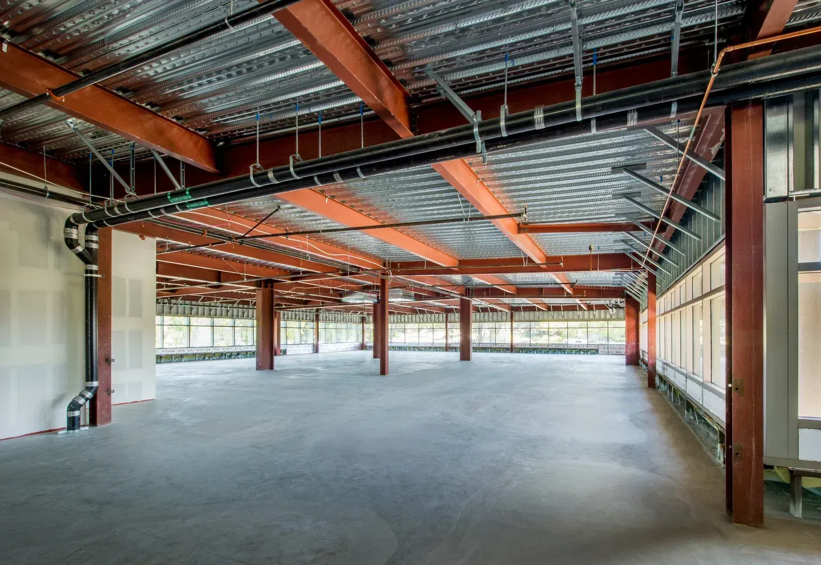 Empty industrial warehouse interior with exposed steel beams, concrete floor, and large windows