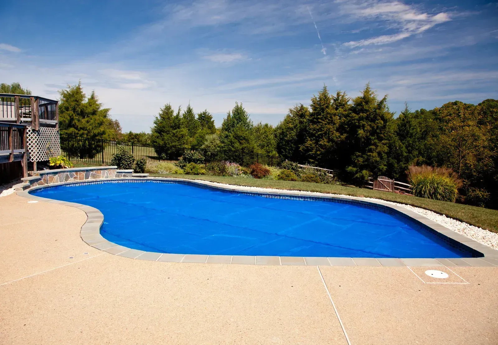 Covered outdoor swimming pool beside a wooden deck and trees under a sunny sky