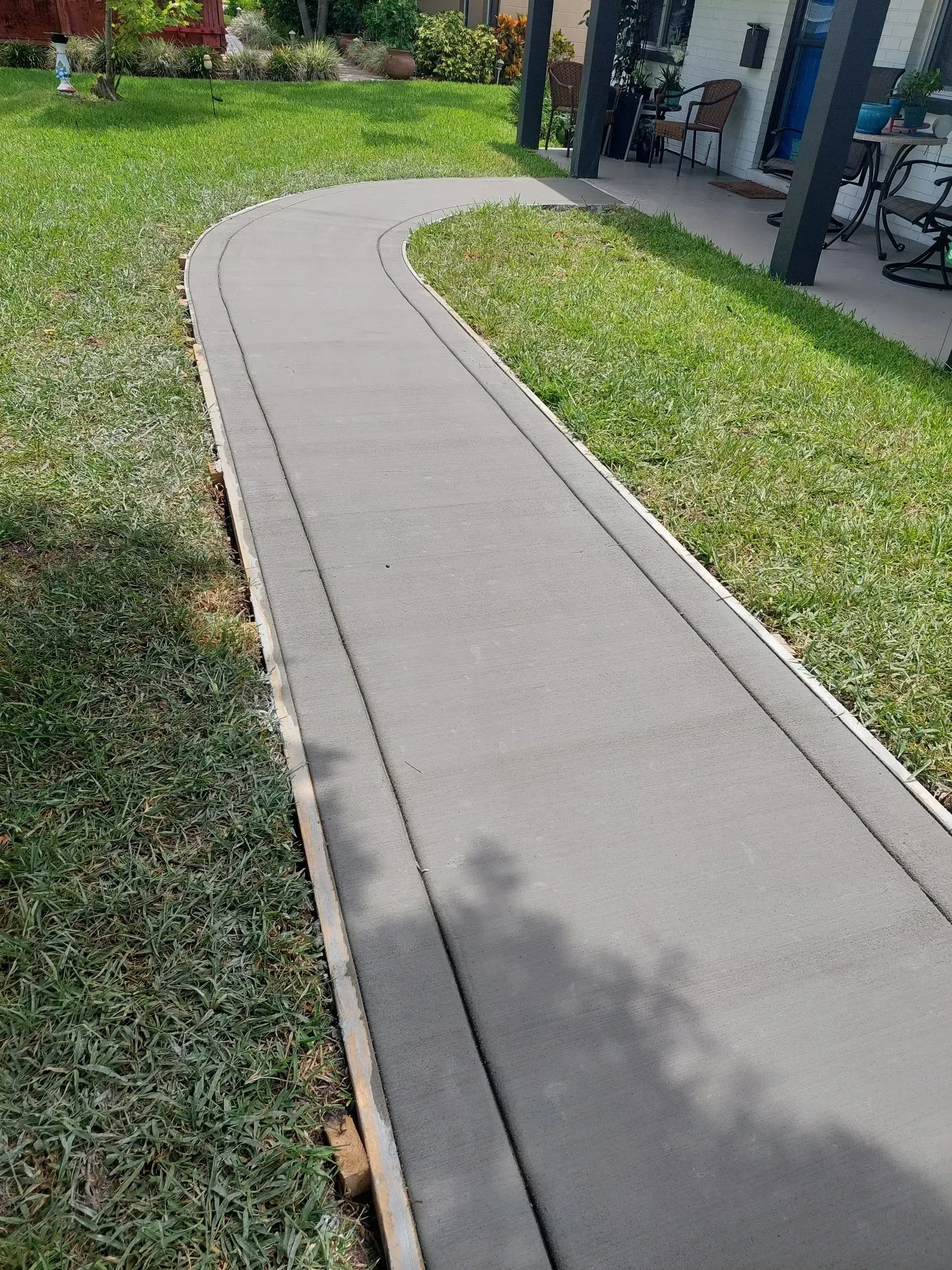 Curved concrete sidewalk beside green grass and a building in daylight