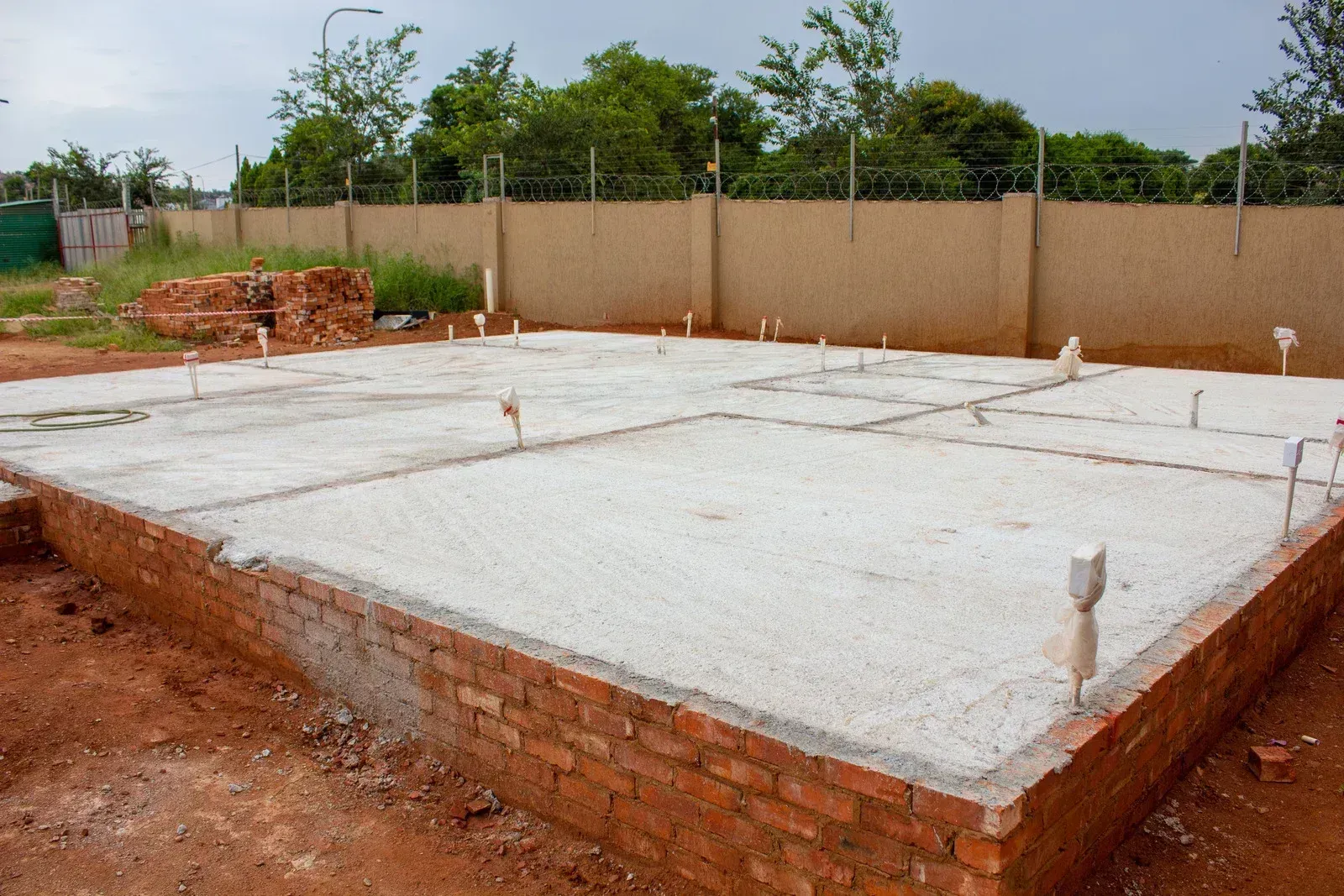 New concrete house foundation on a construction site, surrounded by red soil and a fence