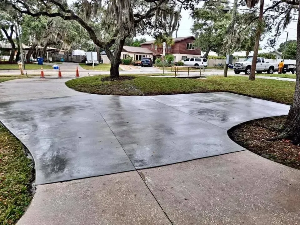Wet concrete walkway and driveway beside a grassy courtyard with trees and parked cars.