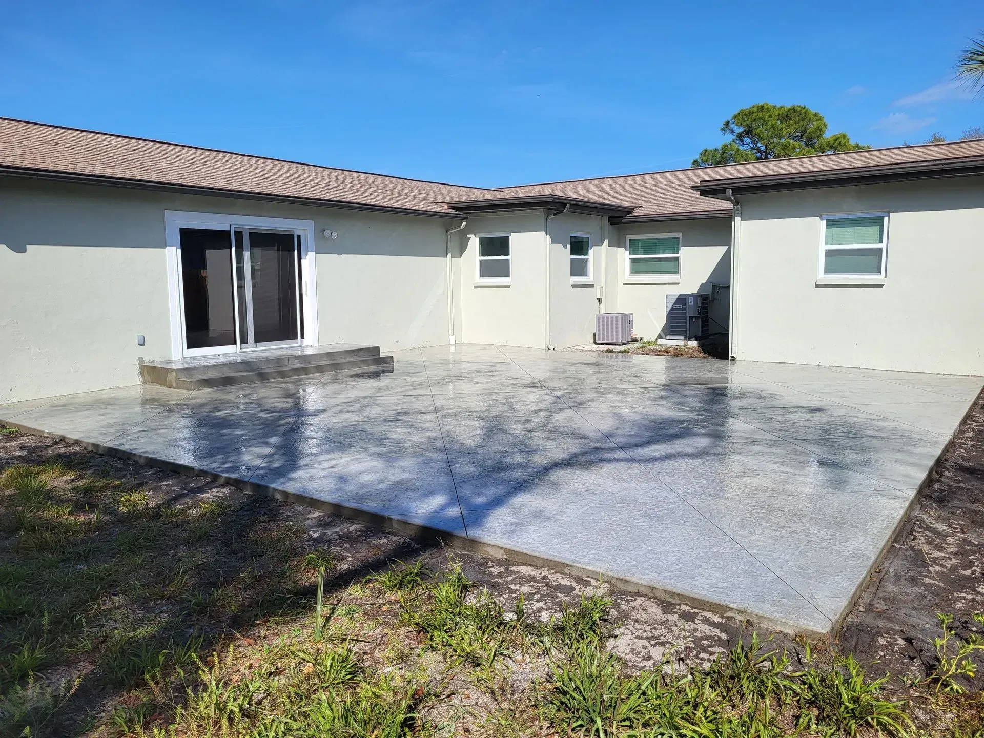Back patio with light gray concrete and sliding glass doors on a beige house