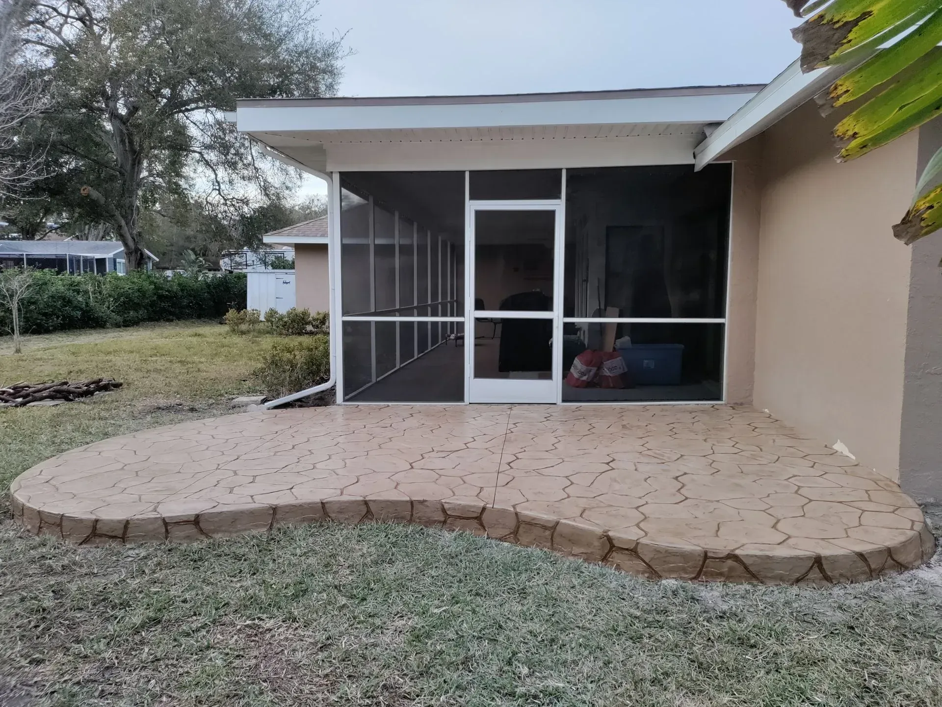 Small screened patio with stone patio floor beside a beige house and grassy yard.