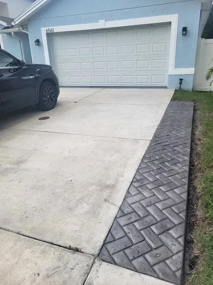 Driveway with a white garage and a black car parked on the left, bordered by a brick walkway.