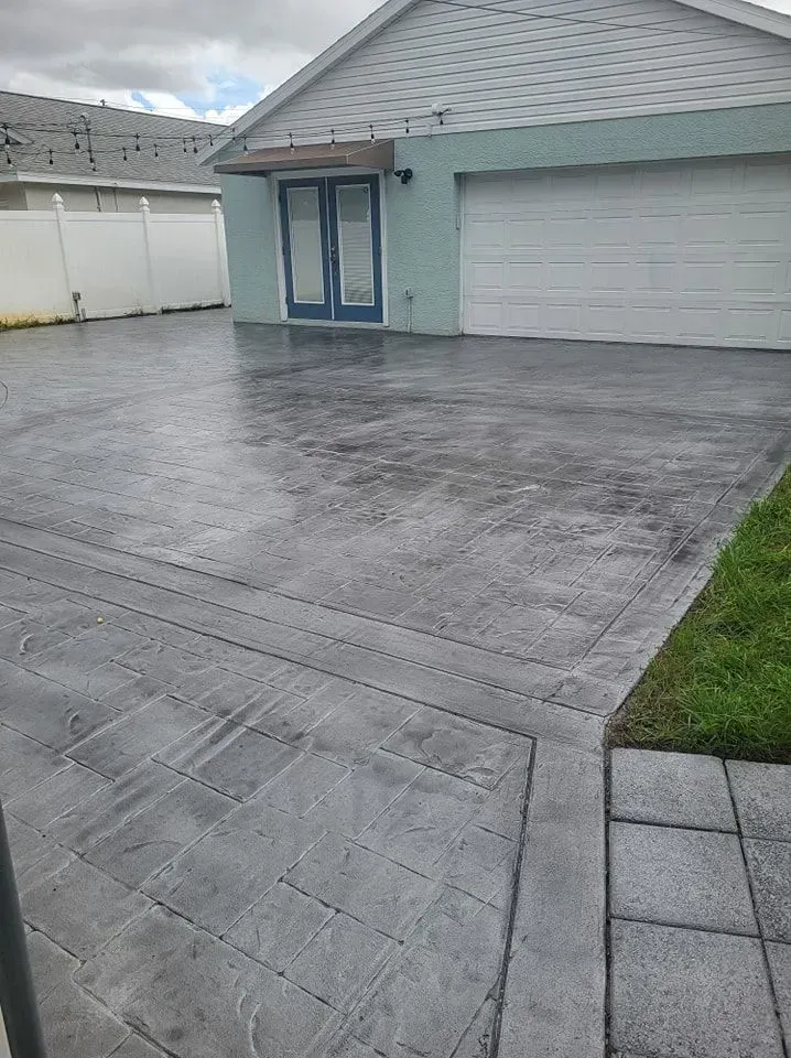 Concrete driveway leading to a two-car garage beside a small patch of grass and pavers.
