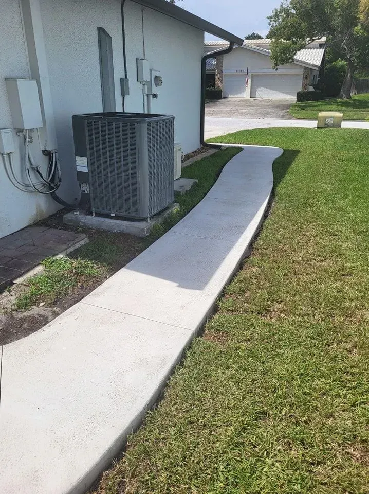 Concrete walkway beside house with an air conditioning unit and green lawn