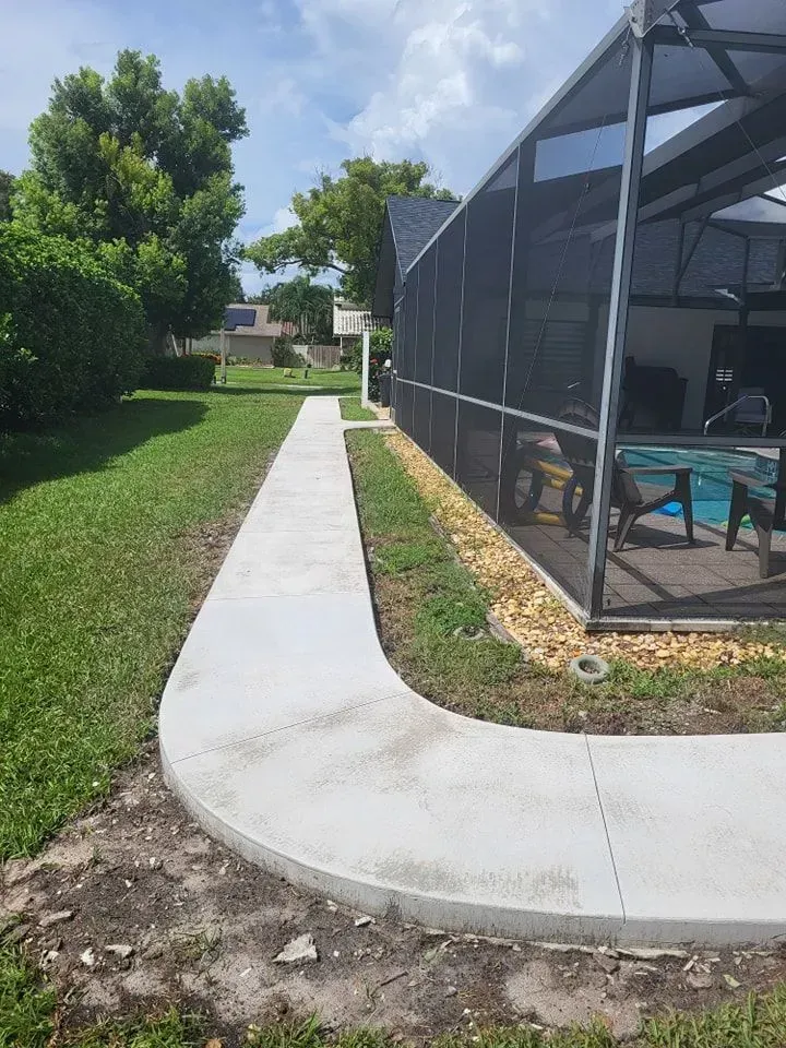 Curved concrete walkway beside a screened patio and green lawn on a sunny day