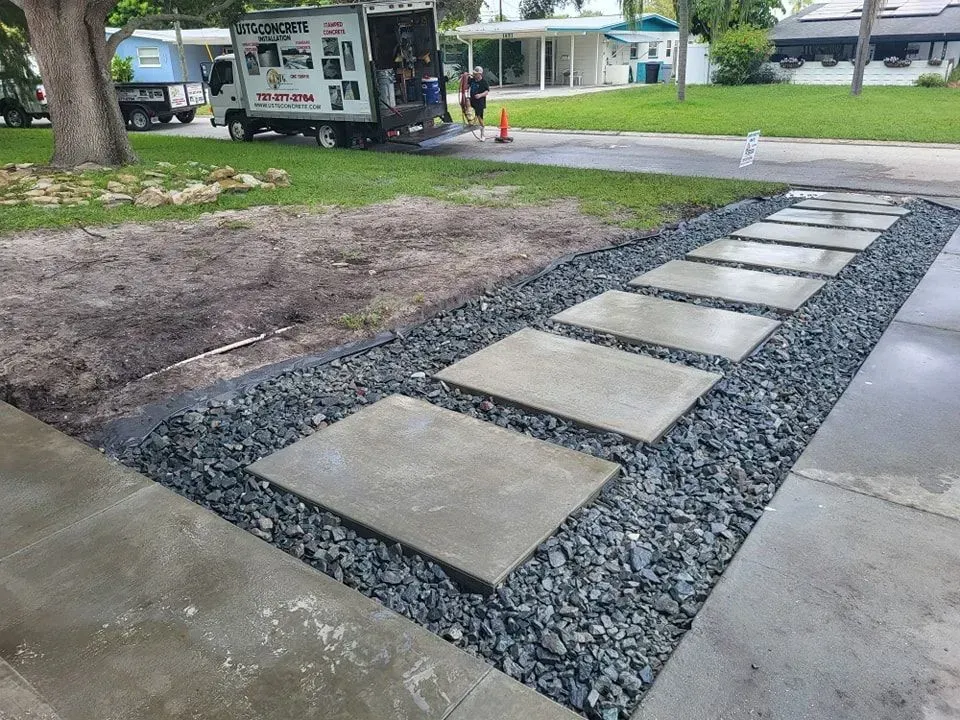 Concrete stepping stones in a gravel path beside a sidewalk and yard, with a utility truck in the background