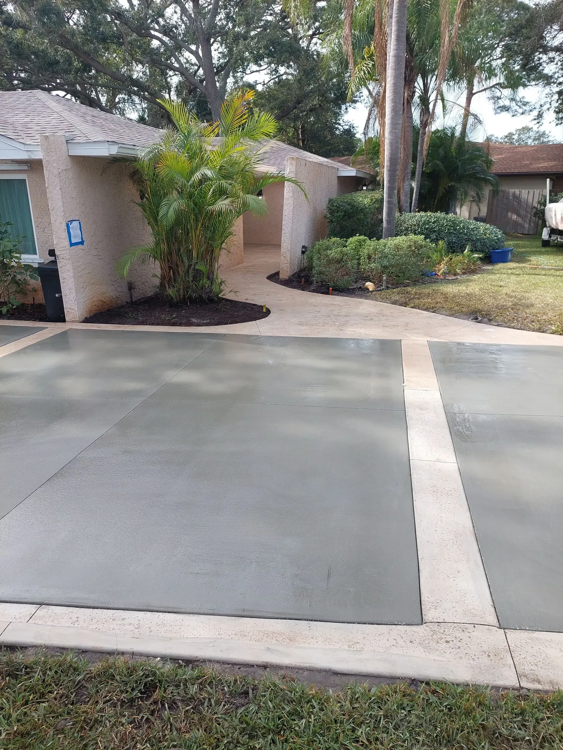 Driveway and front yard of a suburban home with a concrete path, shrubs, and trees.