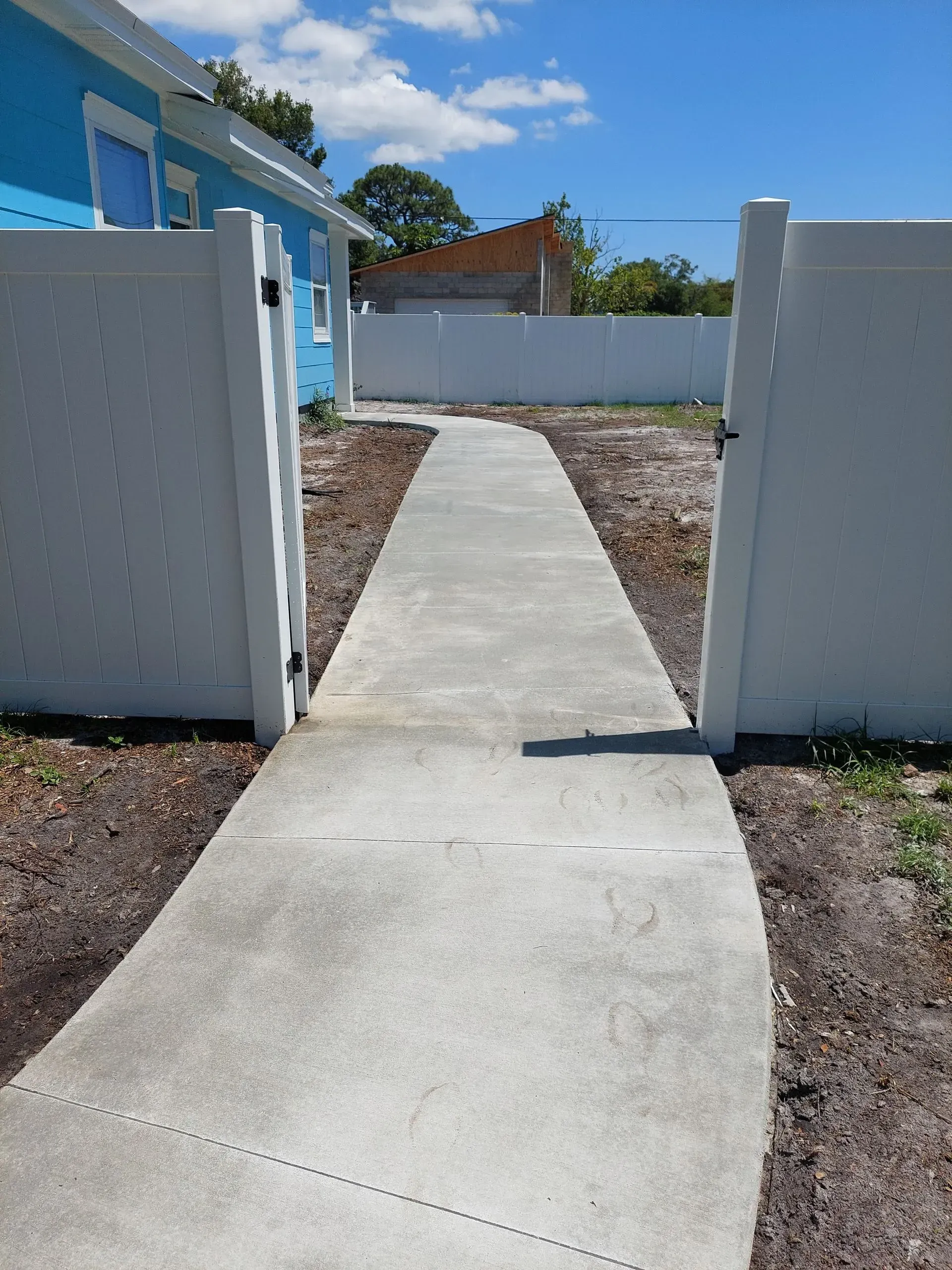 Concrete walkway through white walls leading to a blue house under a clear sky