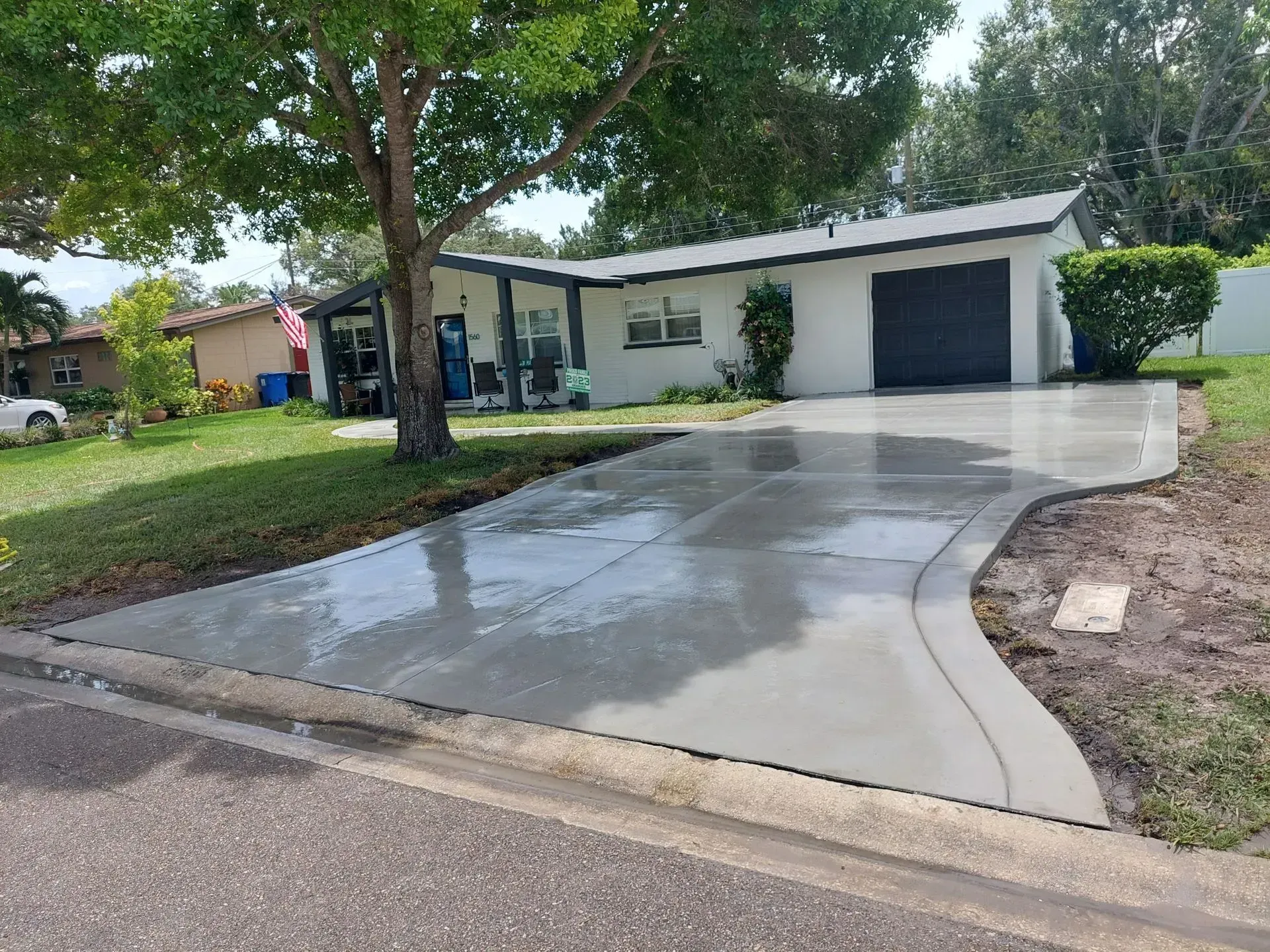 Residential house with wet concrete driveway, single-car garage, and large tree in the front yard.