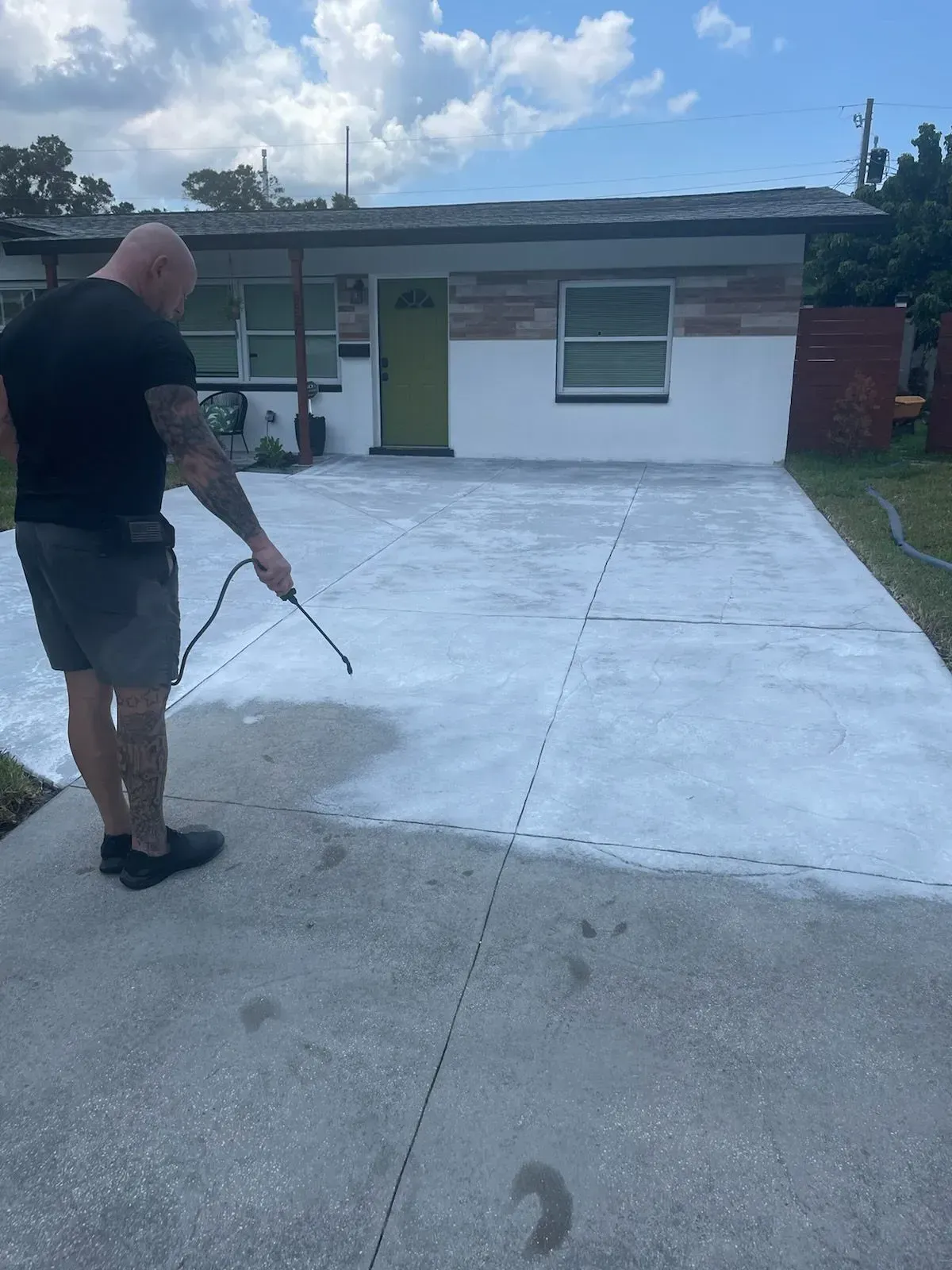 Person pressure-washing a large concrete driveway in front of a small house.