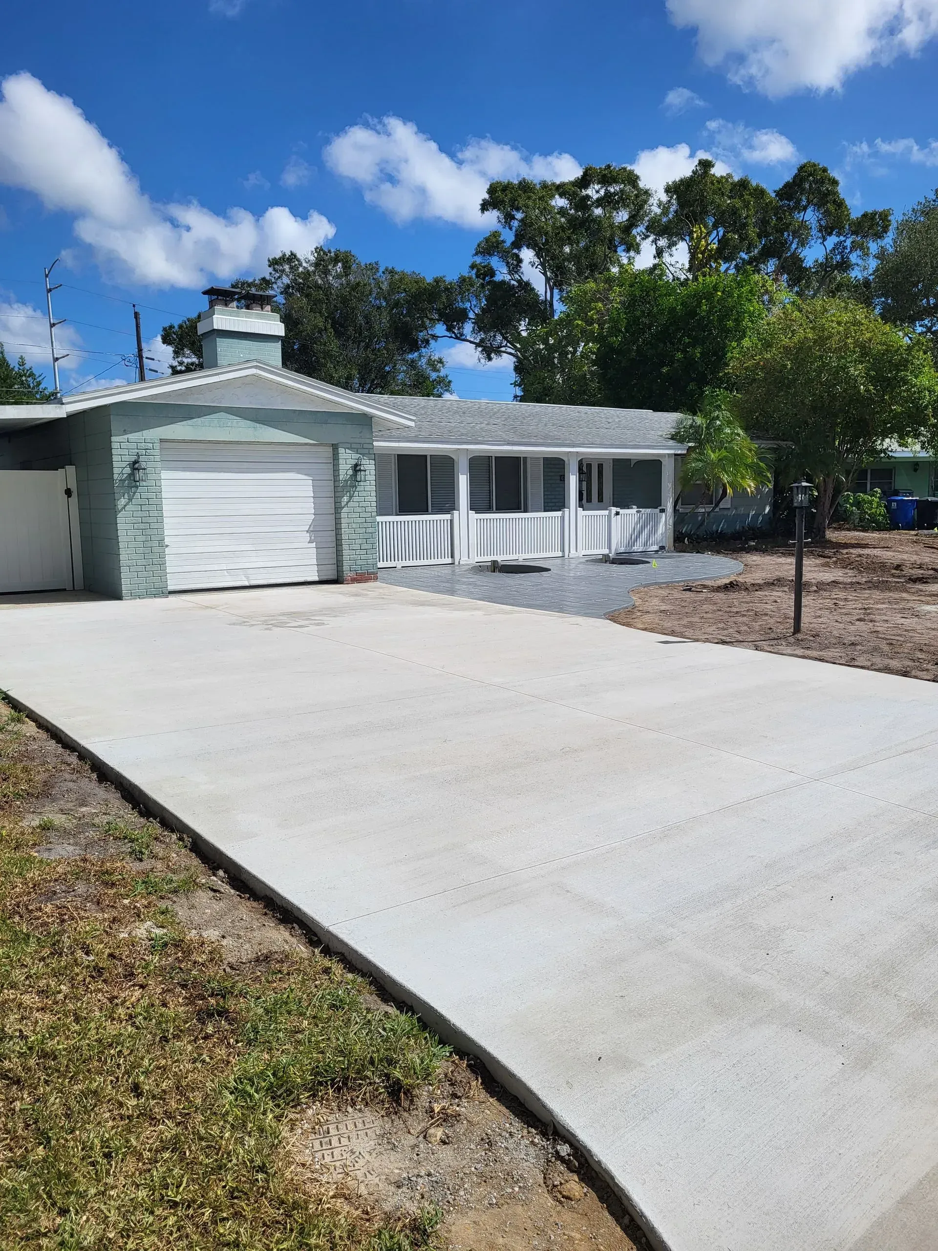 Single-story white house with a large concrete driveway under a blue sky