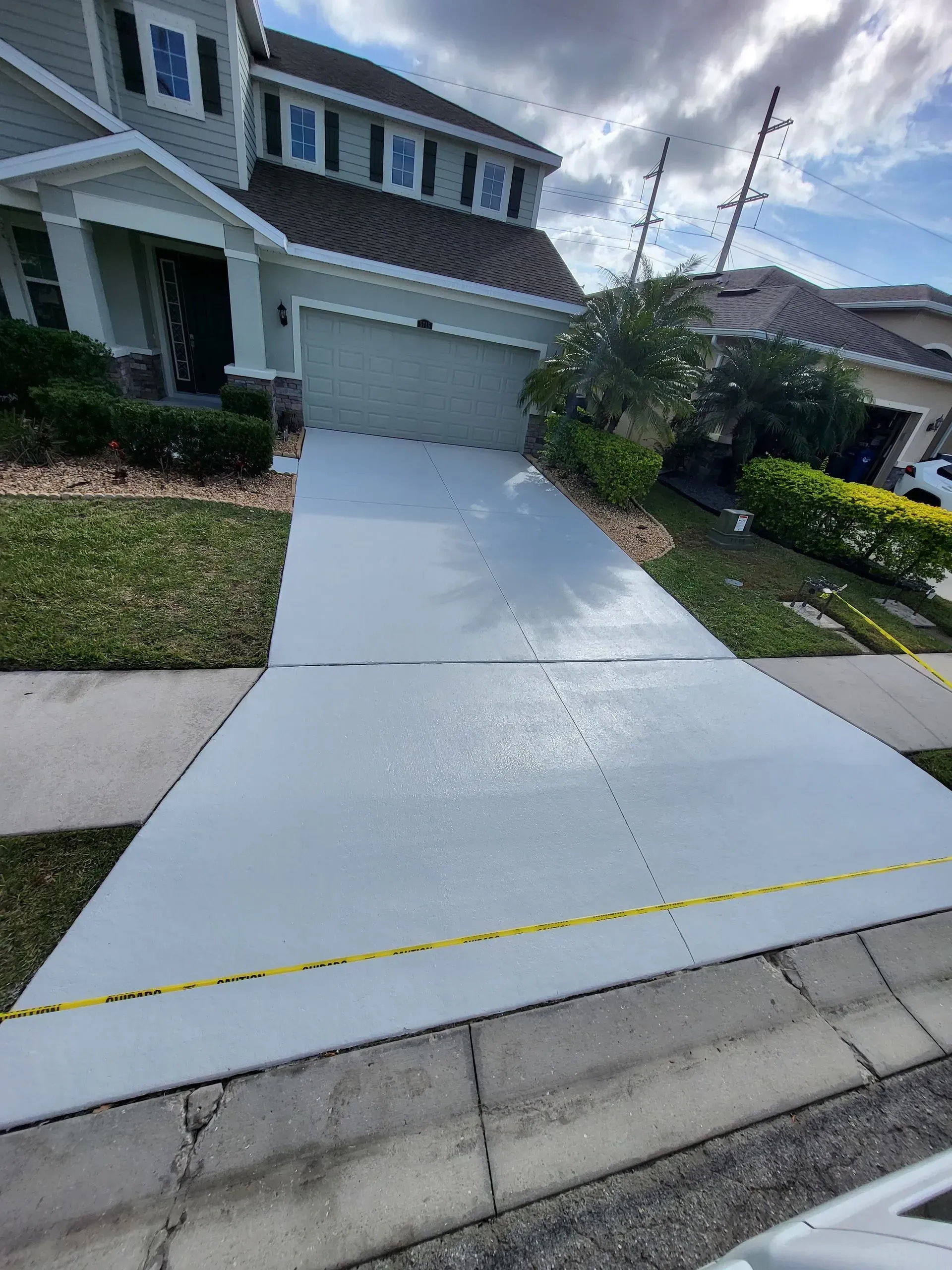 Freshly poured concrete driveway leading to a garage in a suburban home, with a yellow tape across the front edge