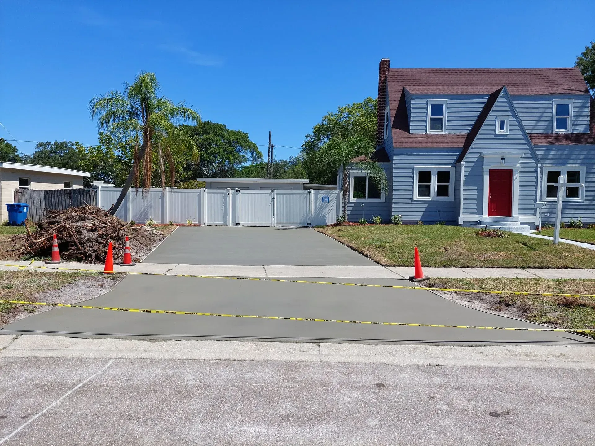 Driveway under construction with orange cones and caution tape in front of a blue house and garage.
