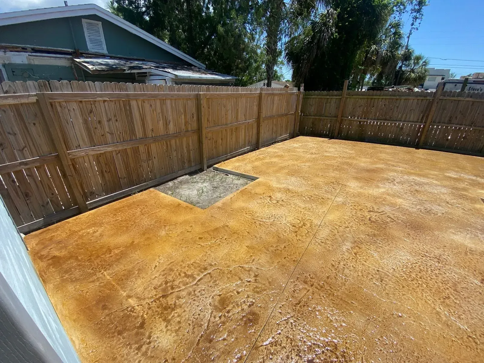 Backyard with wooden fence, dry dirt ground, and a small concrete patch under a sunny sky