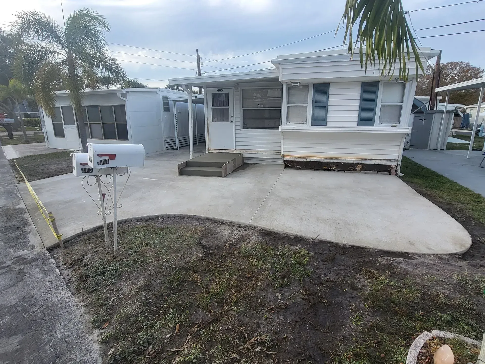White mobile home with a curved concrete driveway and mailbox in a quiet residential lot