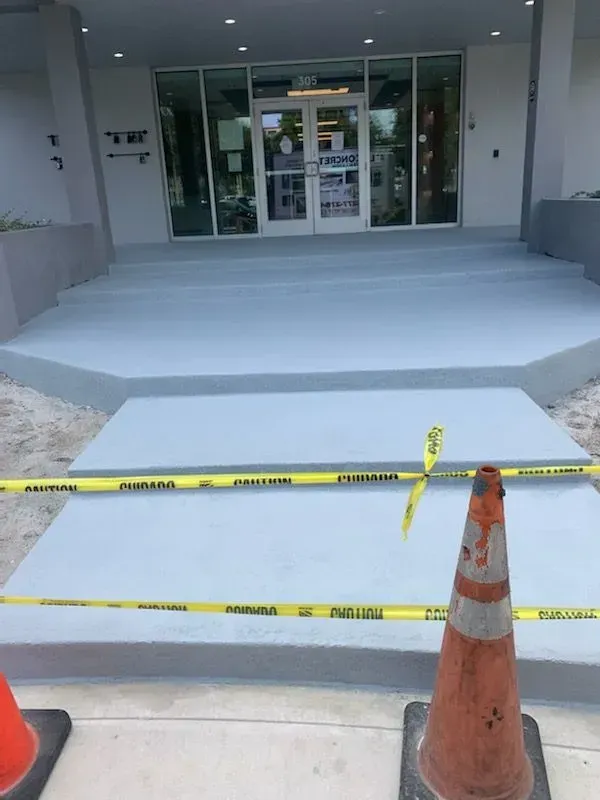 Blocked building entrance with caution tape and traffic cones over a freshly poured concrete ramp