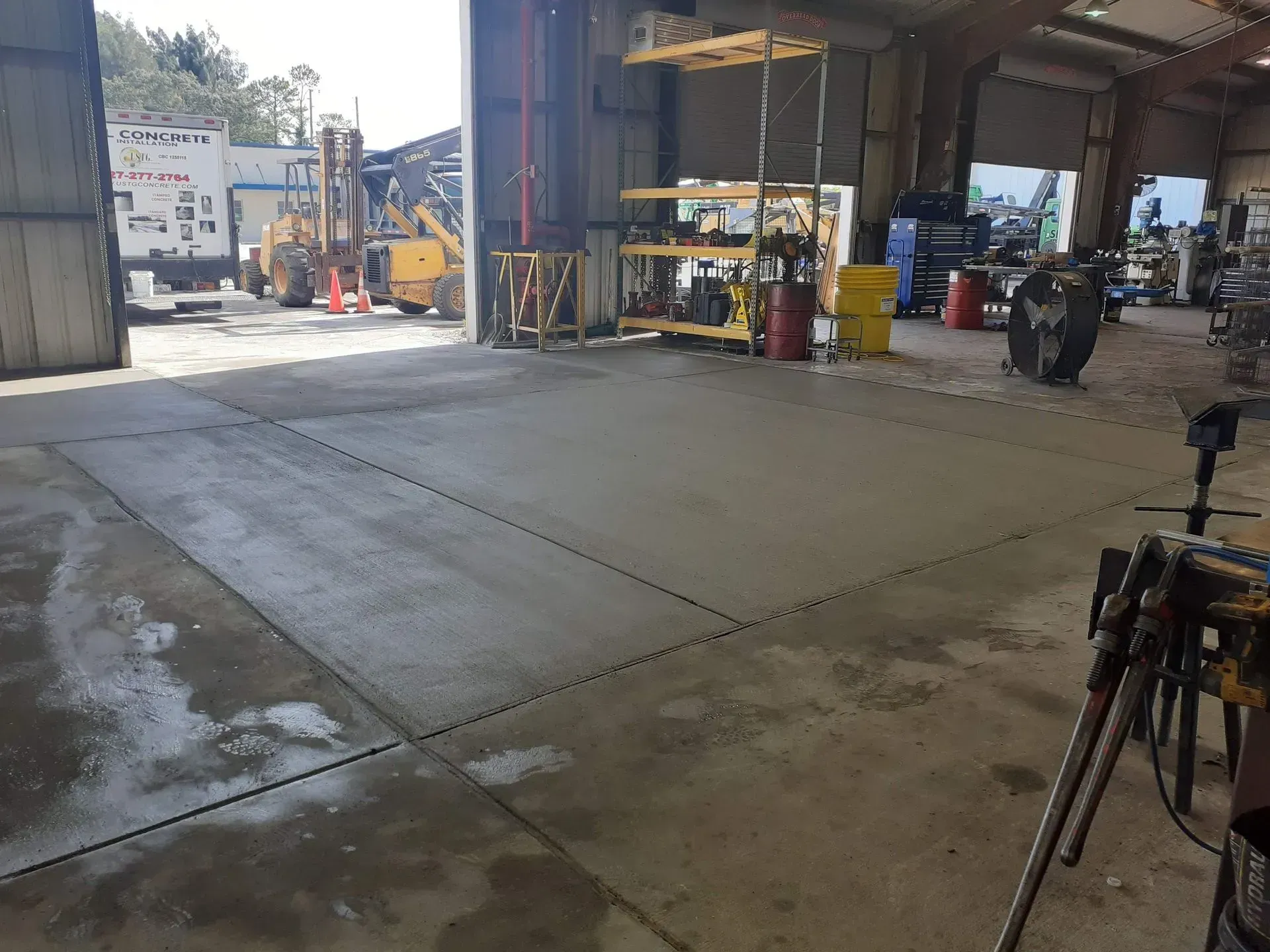 Open industrial garage with concrete floor, equipment, and a motorcycle near the entrance.