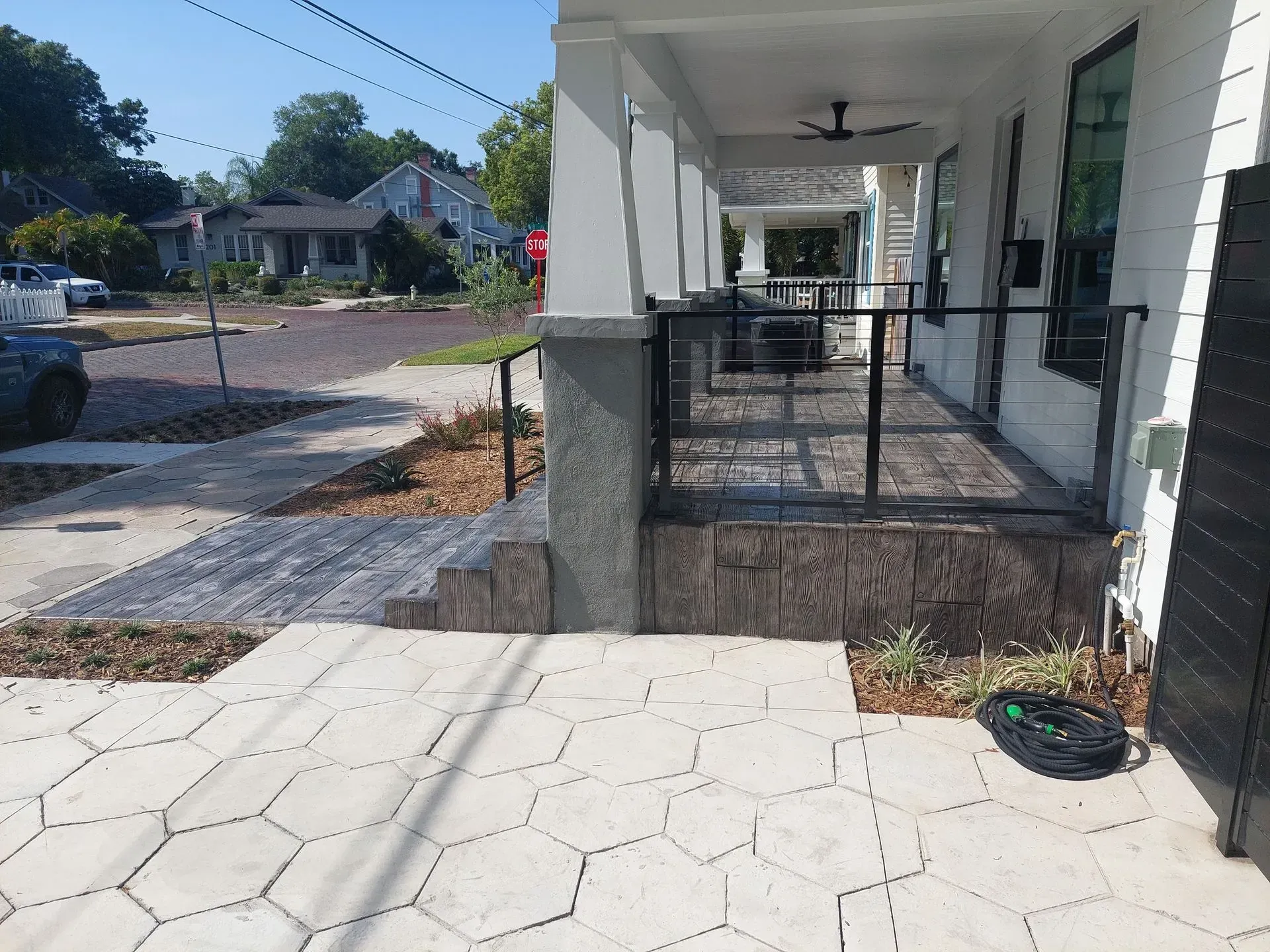 Covered walkway with white columns and black railings beside a tiled sidewalk and street.