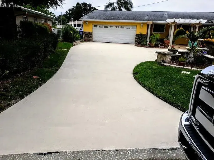 Wide concrete driveway leading to a yellow garage, with a curved landscaped lawn and part of a black truck visible.