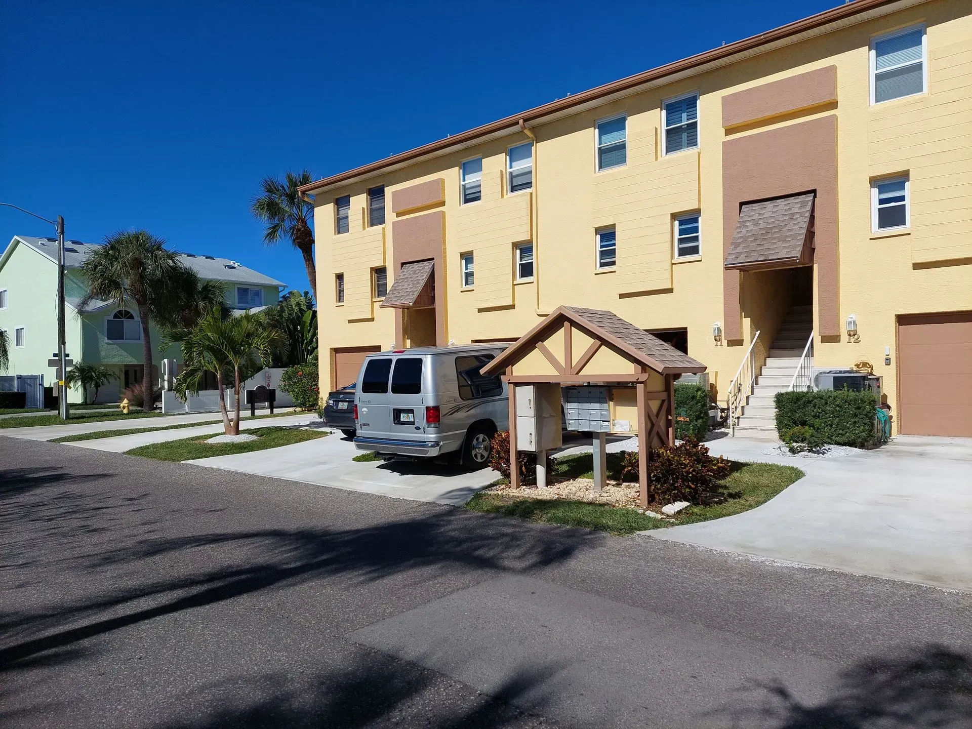 Apartment buildings and parked van beside a small wooden sign under a clear blue sky