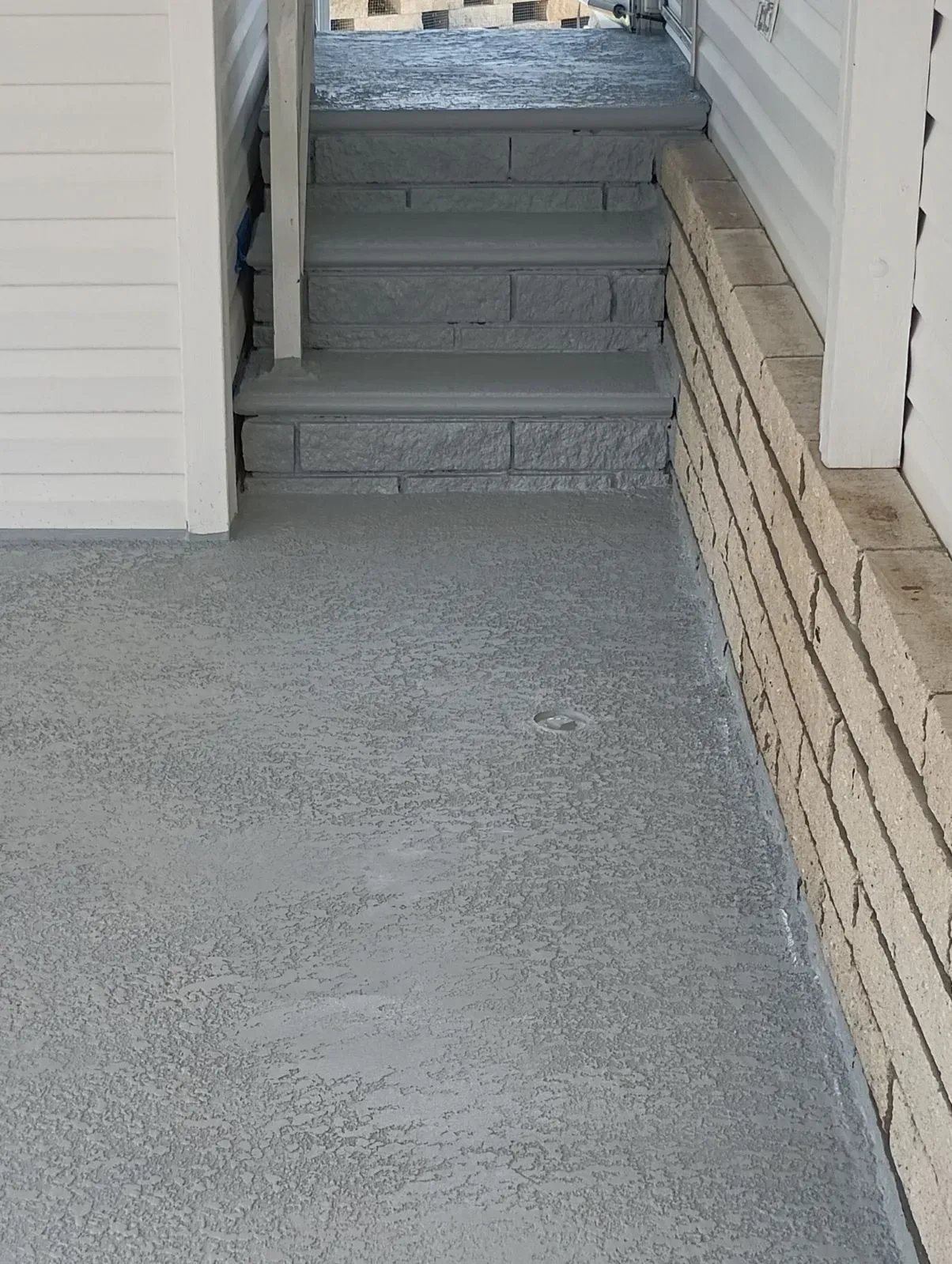 Concrete ramp leading to short steps beside a white building and brick wall