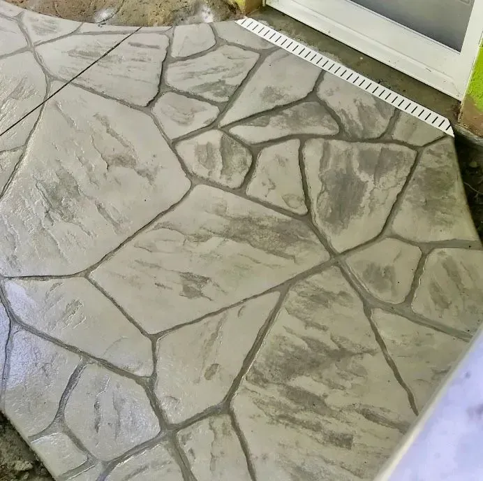 Stone-patterned concrete patio beside a glass door and drain channel