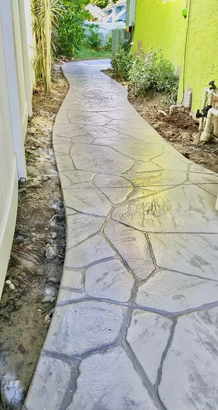 Curved stone walkway between green walls and plants, leading toward a bright outdoor opening.