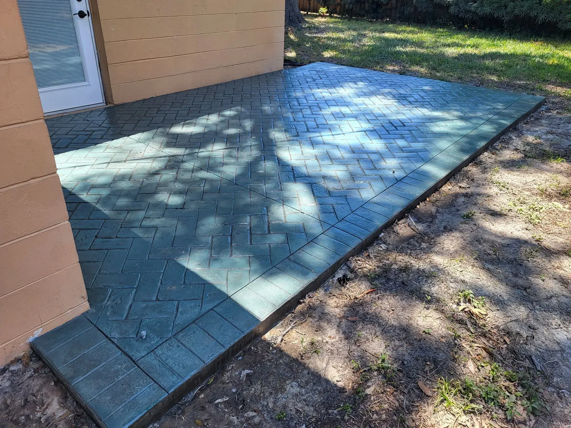 Shaded blue-tiled patio beside a house, bordered by soil and grass.