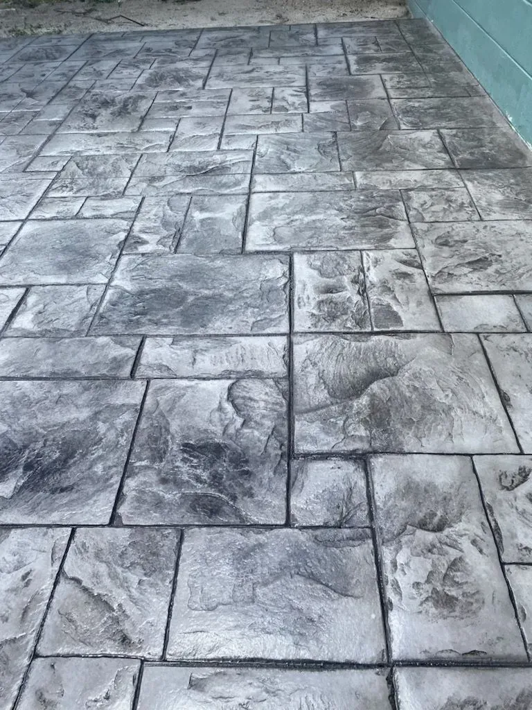 Gray stamped concrete patio with irregular stone pattern and wet-looking patches