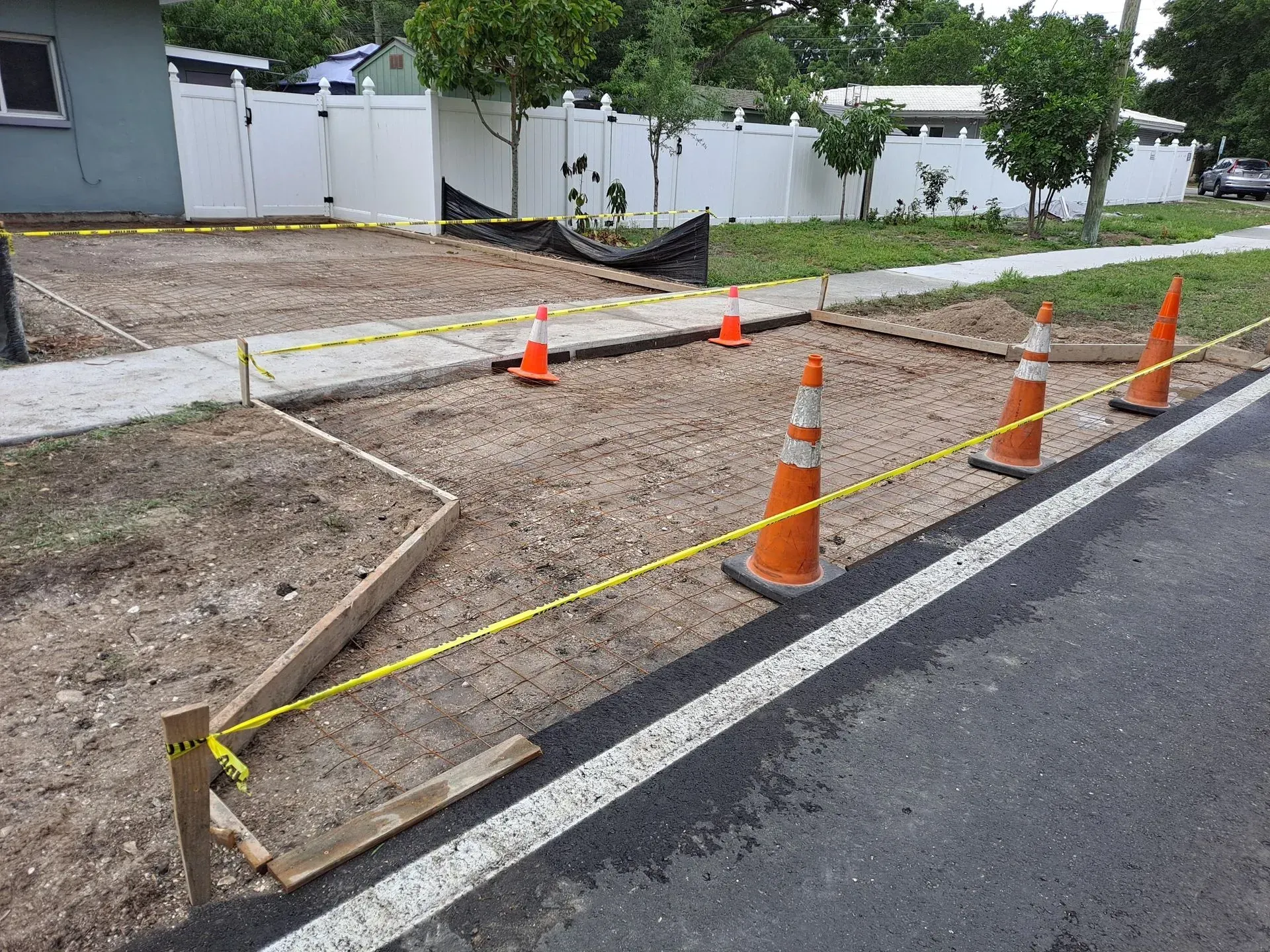 Roadside construction area with orange cones, yellow caution tape, and a gravel trench beside pavement
