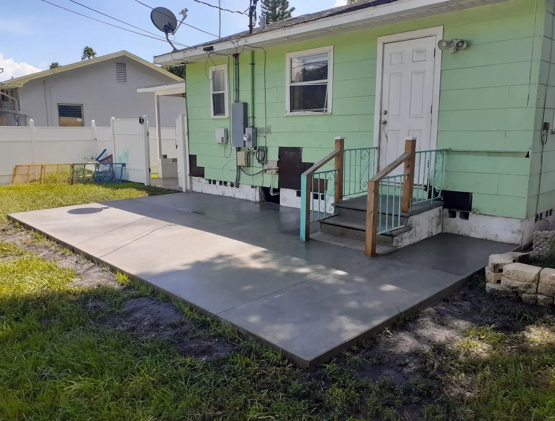 Back porch with concrete ramp leading to a mint-green house door, with steps and utility meters nearby