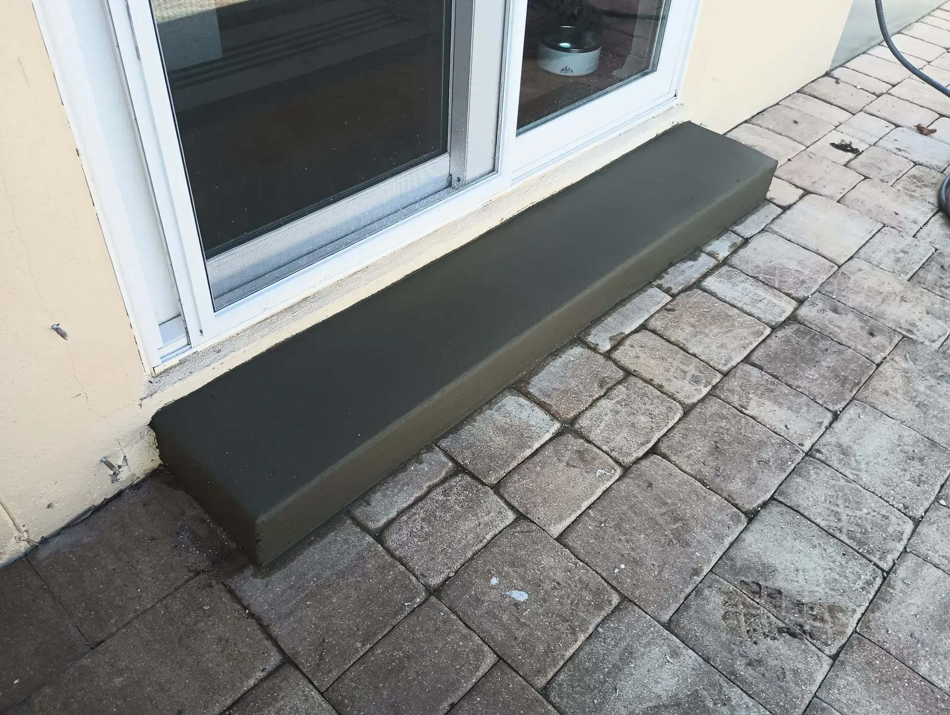 Dark gray bench beneath a sliding glass door on a paved patio