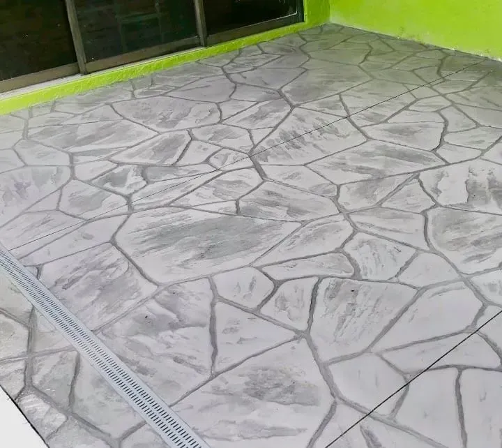 Stamped concrete patio with gray stone pattern and a drainage grate along the edge