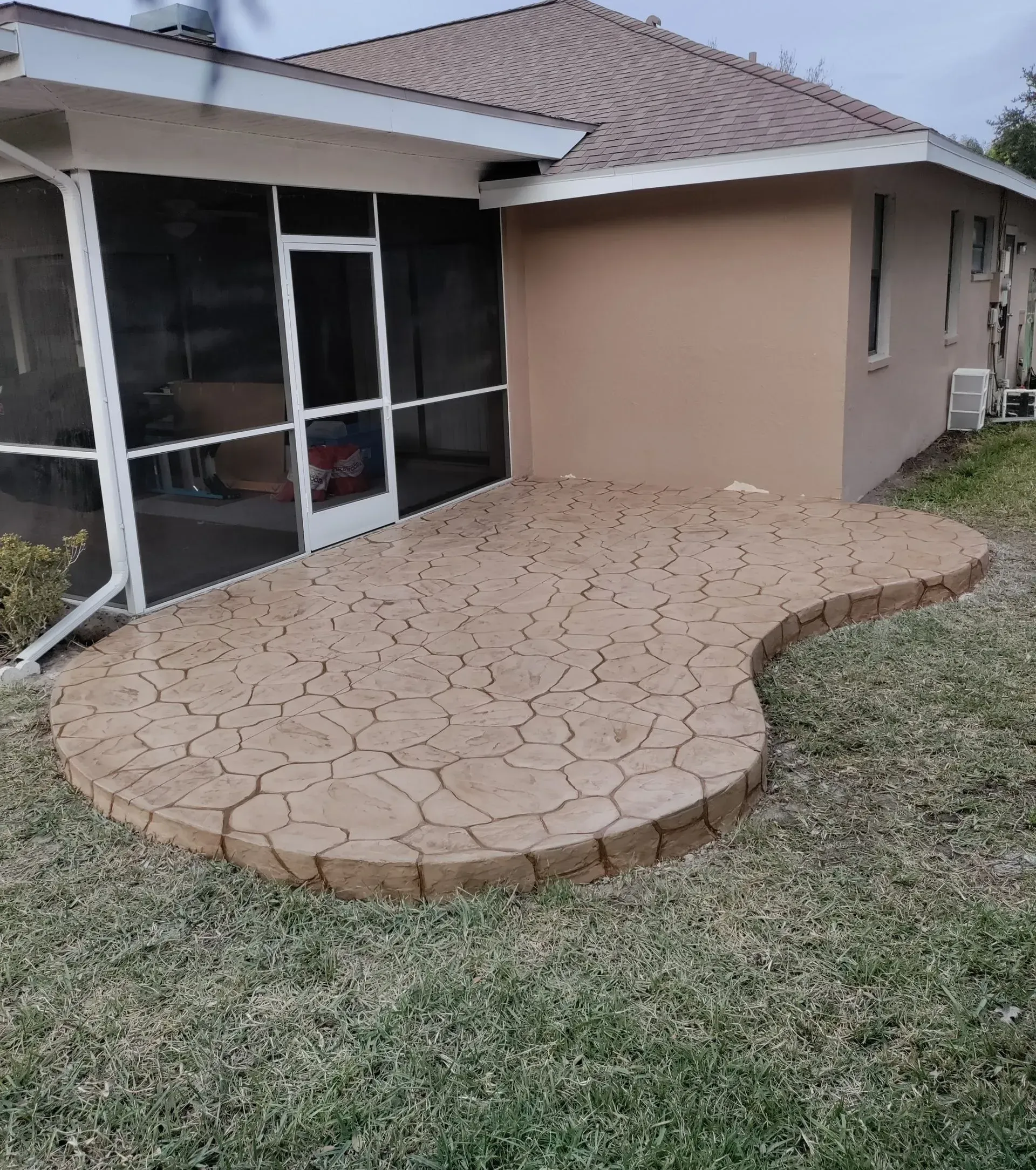 Curved stamped-concrete patio beside a tan house with screened windows and grass yard
