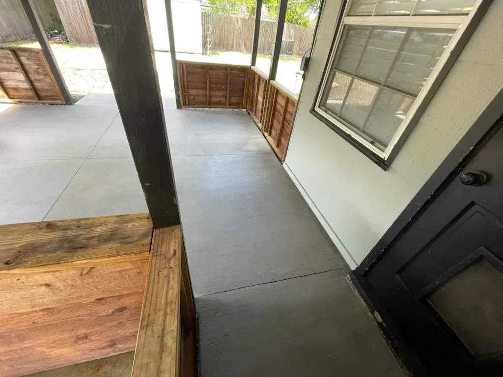 Covered outdoor walkway with concrete floor, black pillars, wood railings, and a dark door beside windows