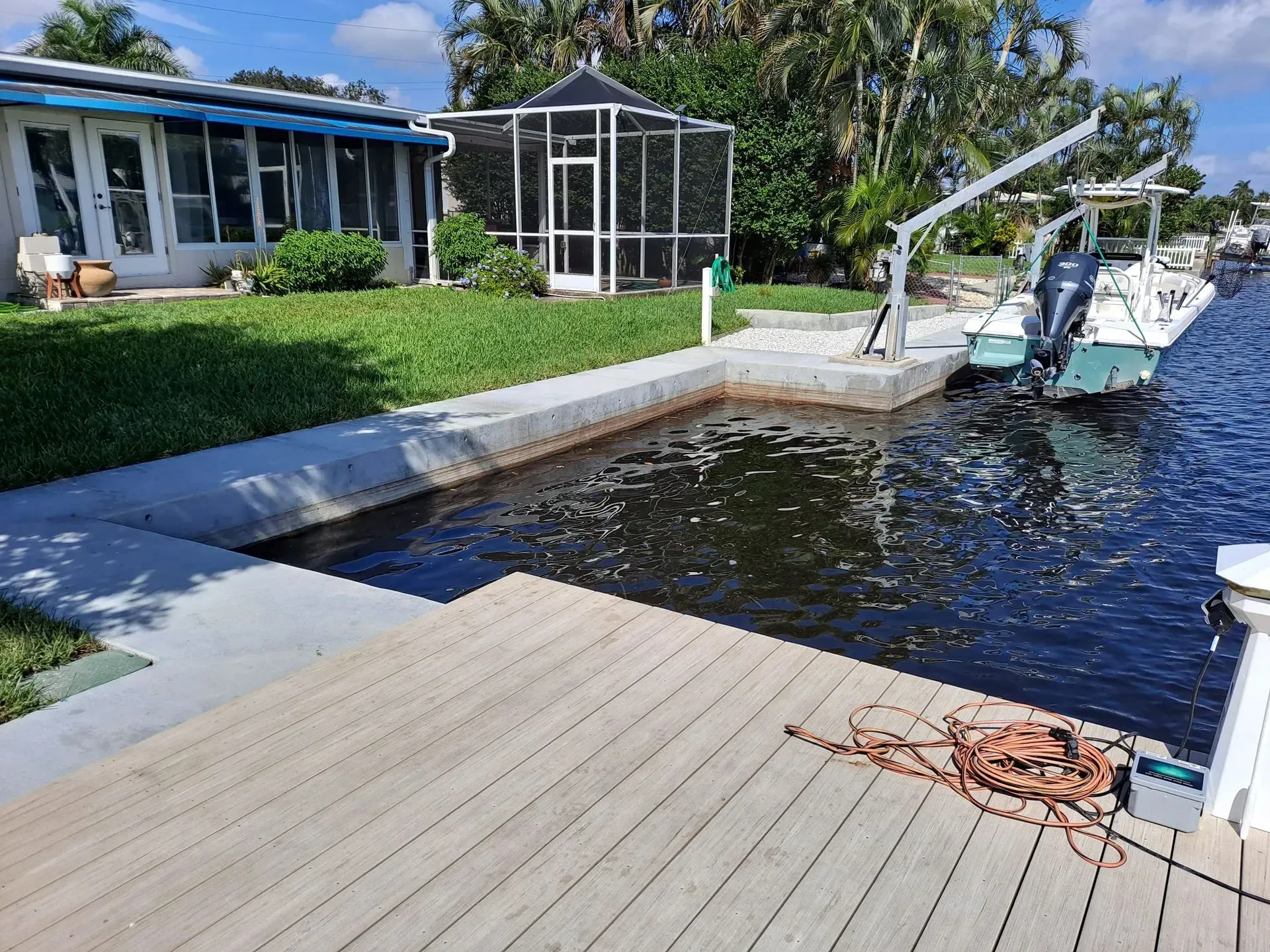 Canal-side dock with a white boat, screened patio, and lush greenery