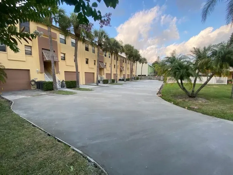 Quiet residential street beside tan apartment buildings with palm trees and a paved driveway under a blue sky