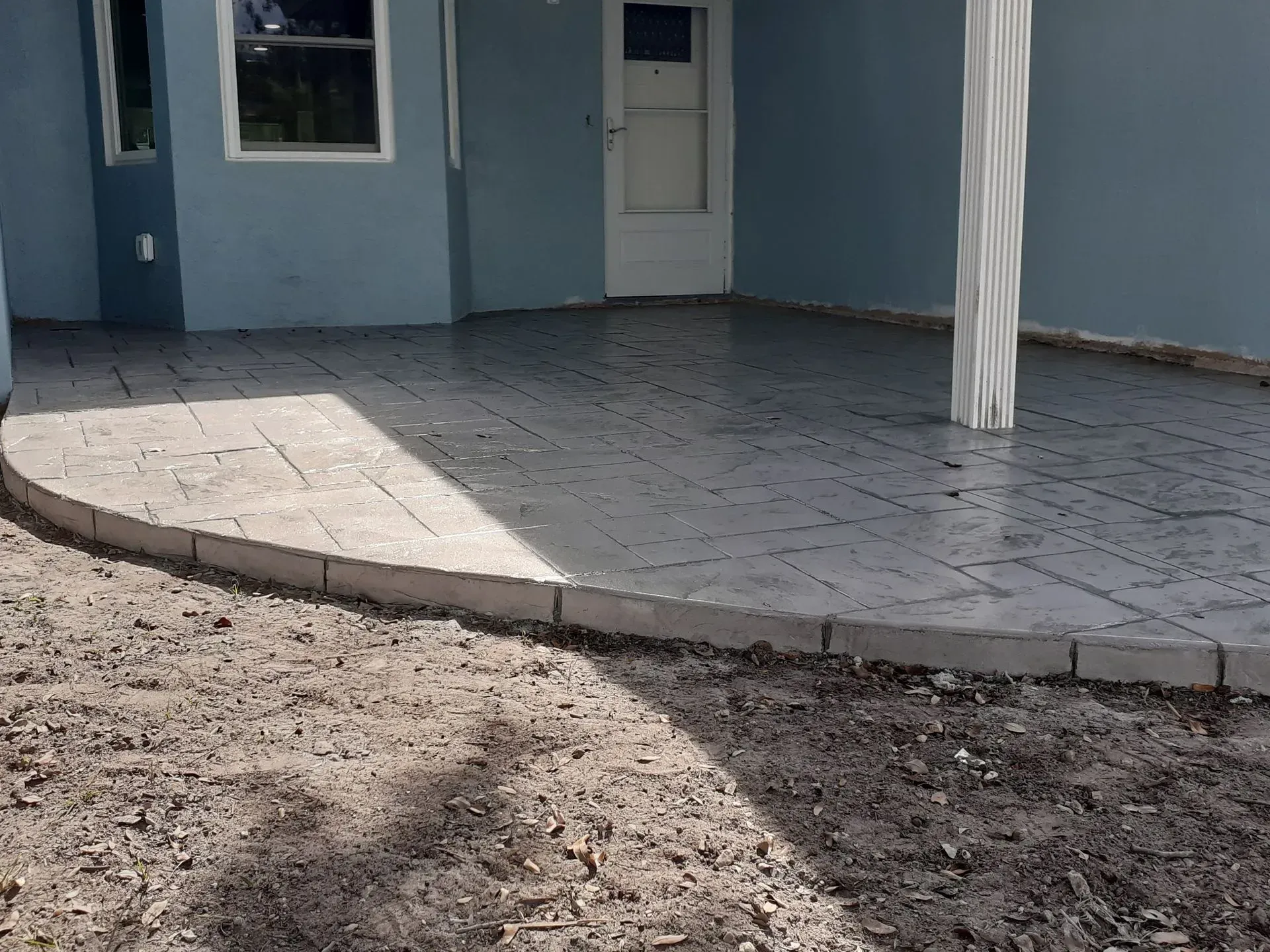 Blue house porch with curved tiled patio, front door, and a dirt yard in the foreground