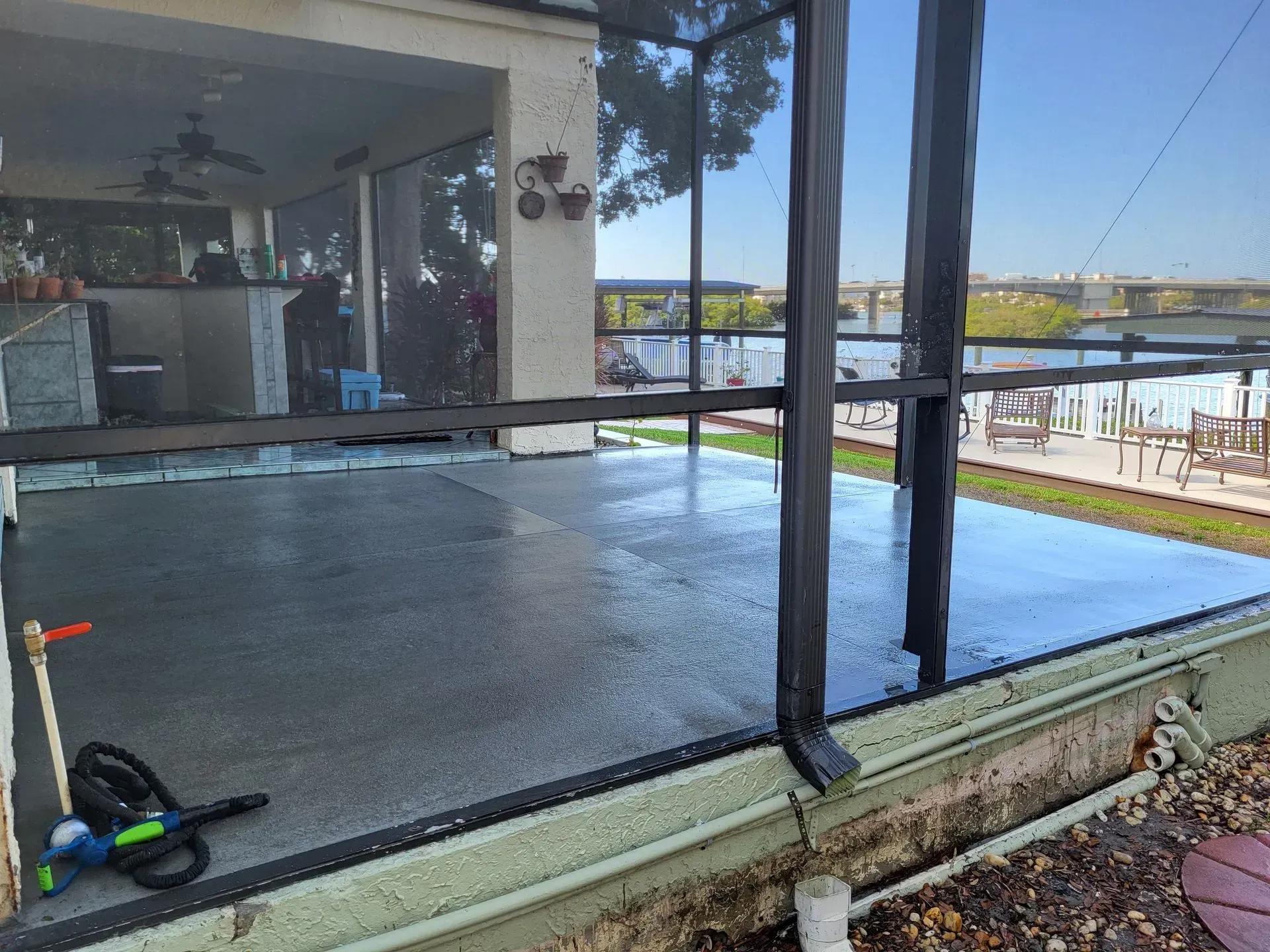 Freshly poured concrete slab beside a glass-walled house, with tools on the floor and a patio beyond.