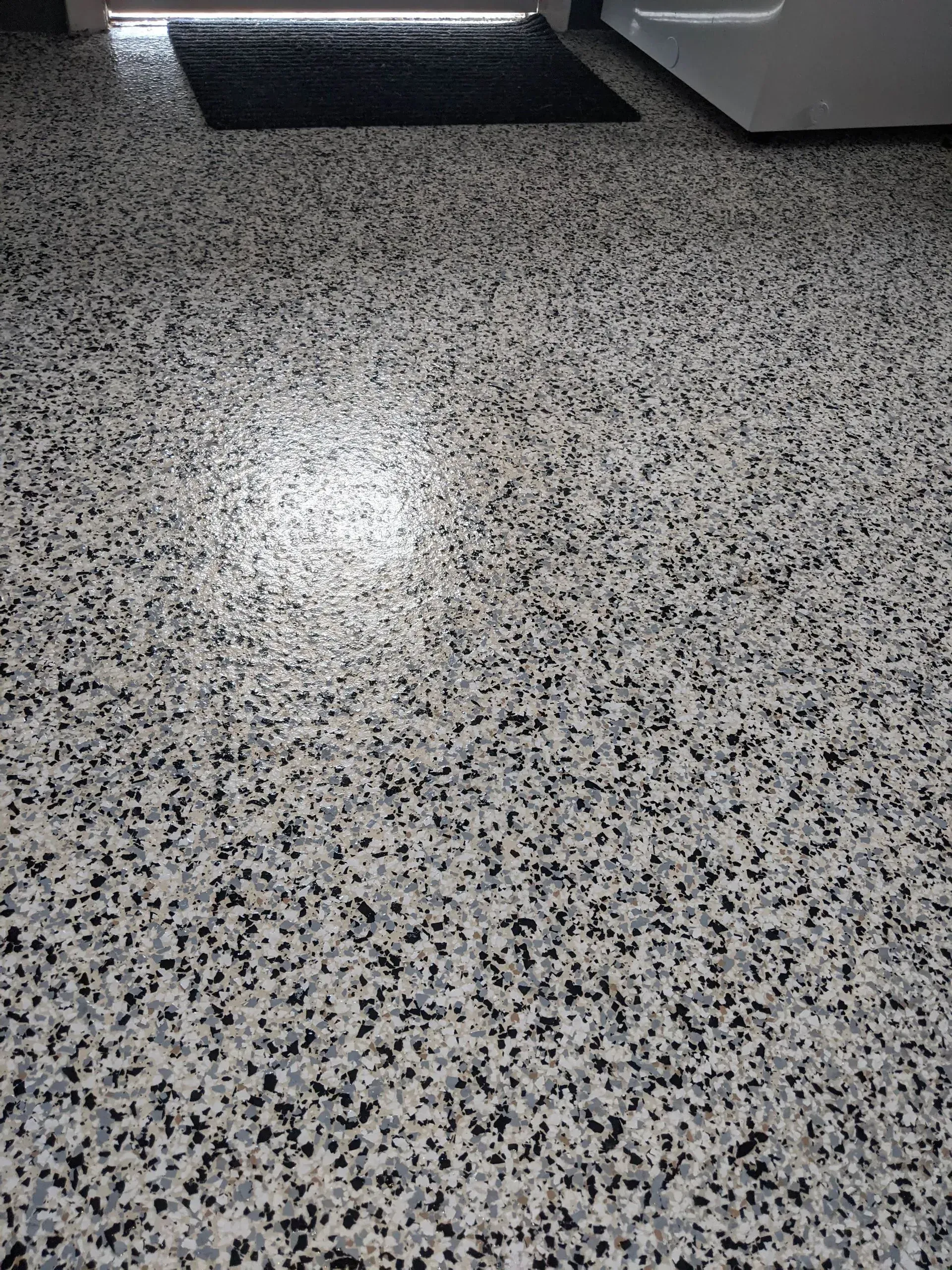 Close-up of a speckled gray granite floor with a bright light reflection.