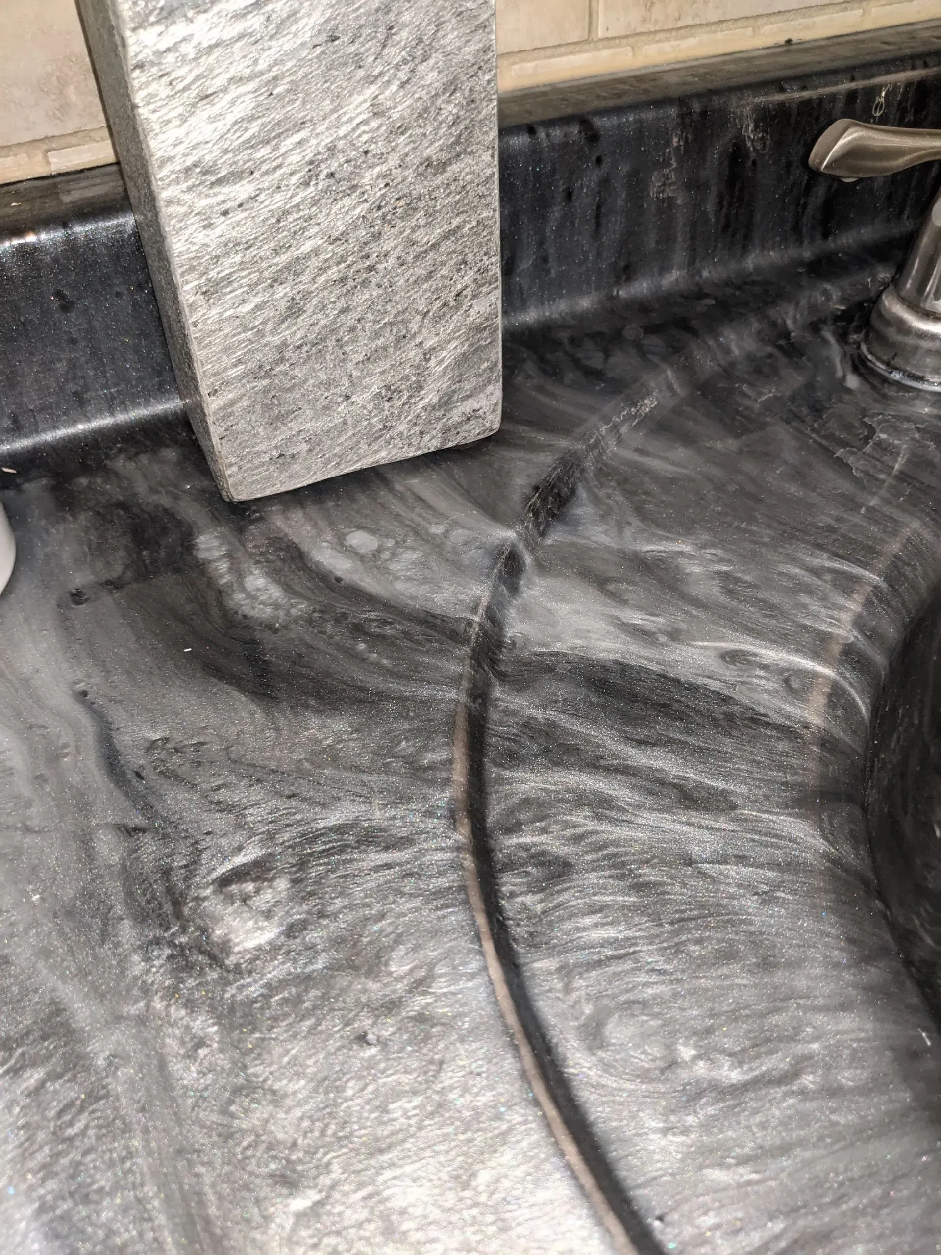 Close-up of a dirty black sink or tub with white streaks and a towel hanging above it