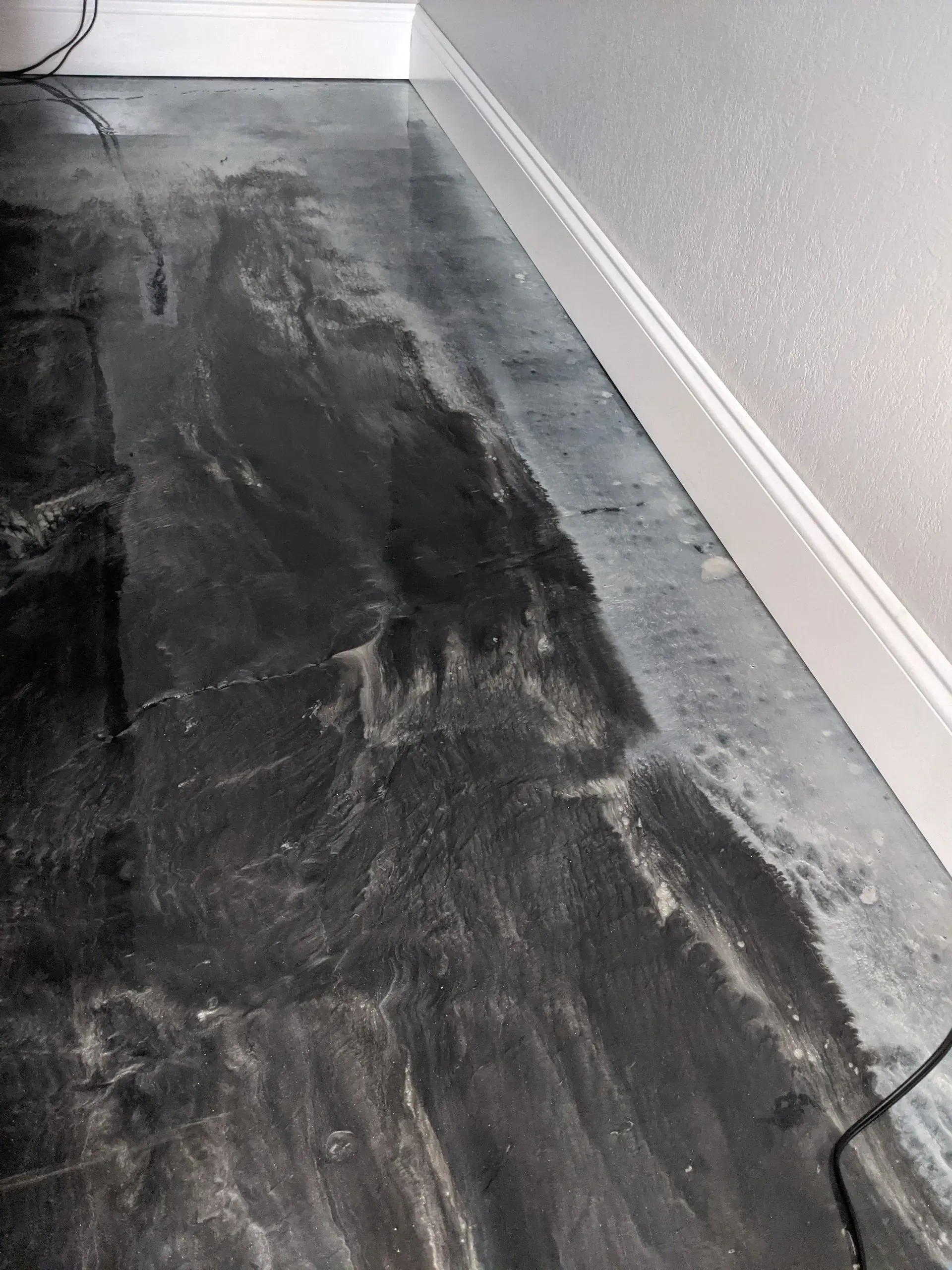 Partially stripped black flooring beside a white wall in an indoor room