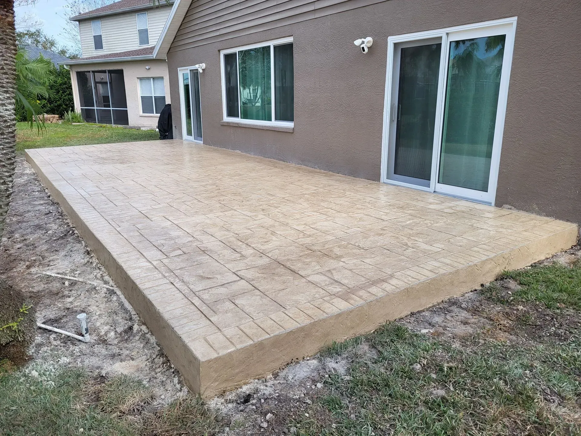 Freshly paved tan concrete patio beside a brown house with sliding glass doors