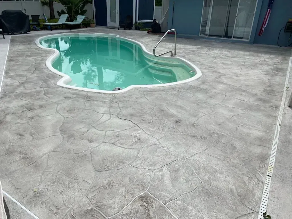 Small turquoise swimming pool in a stamped concrete patio outside a house