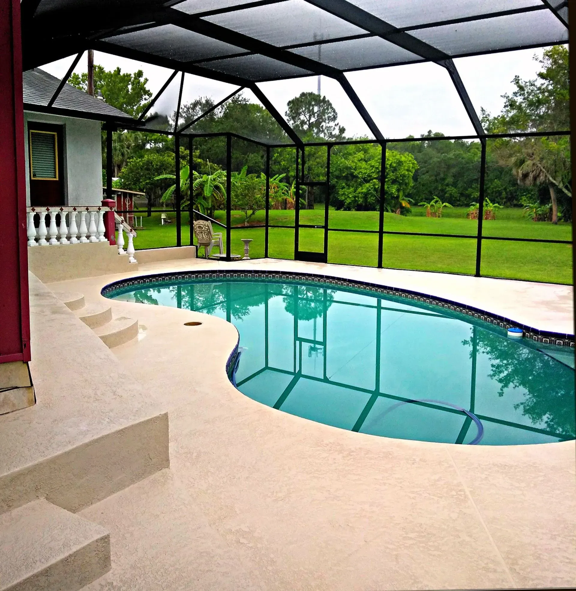 Covered backyard pool with turquoise water beside a screened patio and lush green lawn.