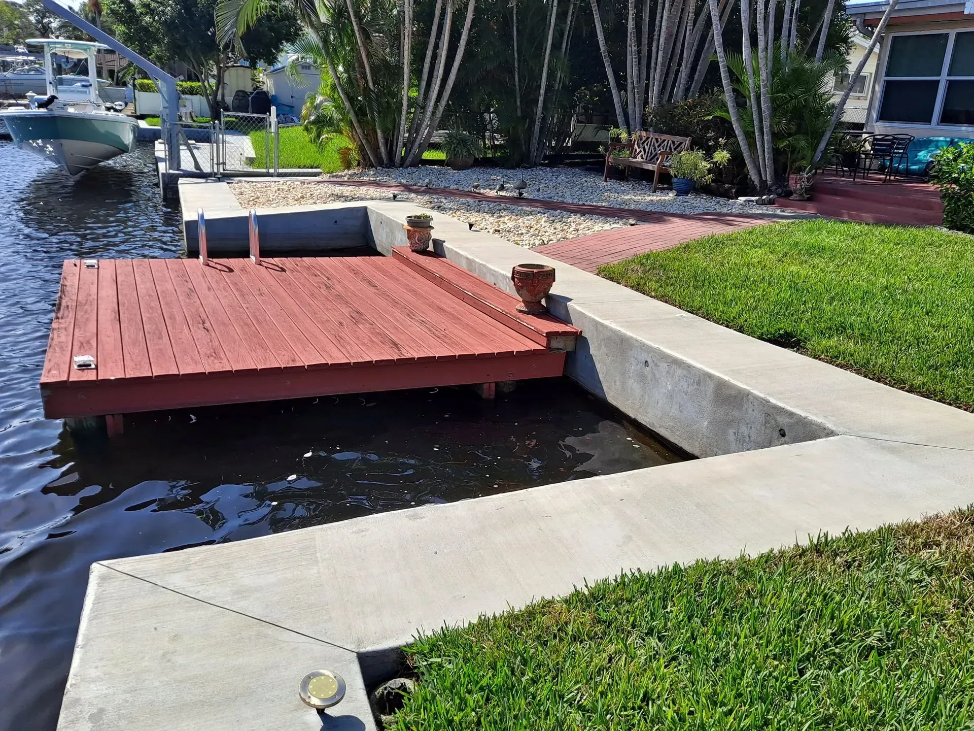 Red dock beside a narrow canal, bordered by concrete edges and green lawn in a landscaped yard