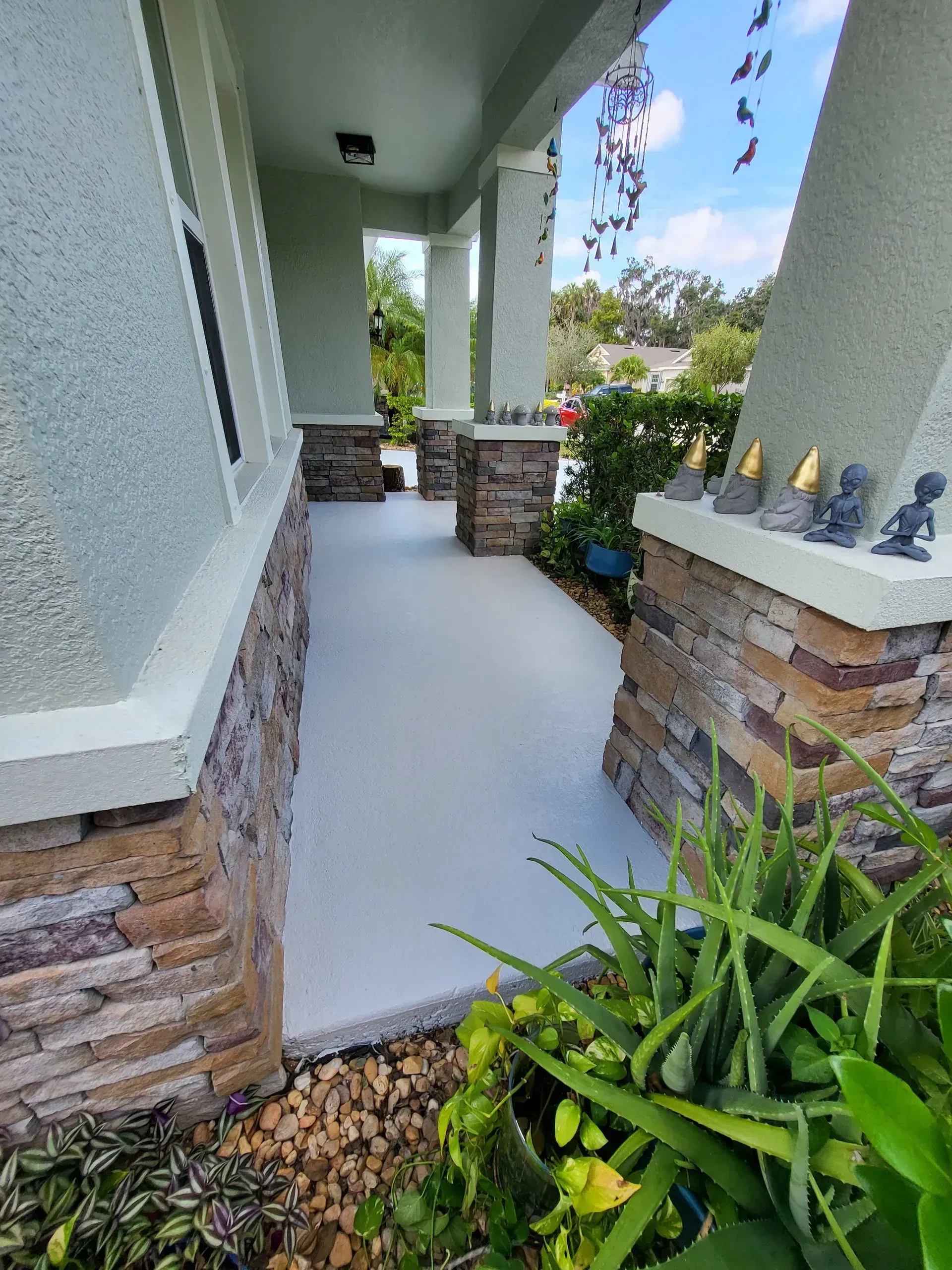 Front porch walkway with white columns, stone accents, and green plants by the entrance